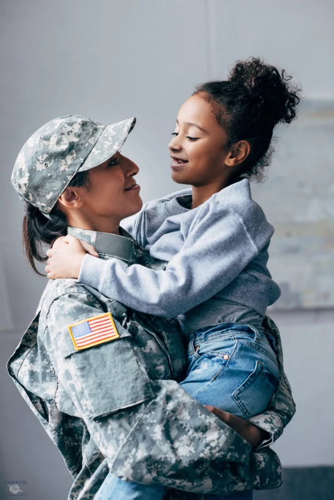 Woman in military uniform holding daughter in arms at home.