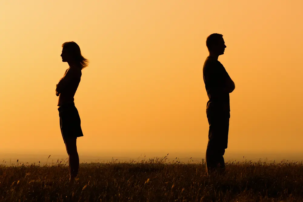 A man and woman facing opposite directions in front of sunset.