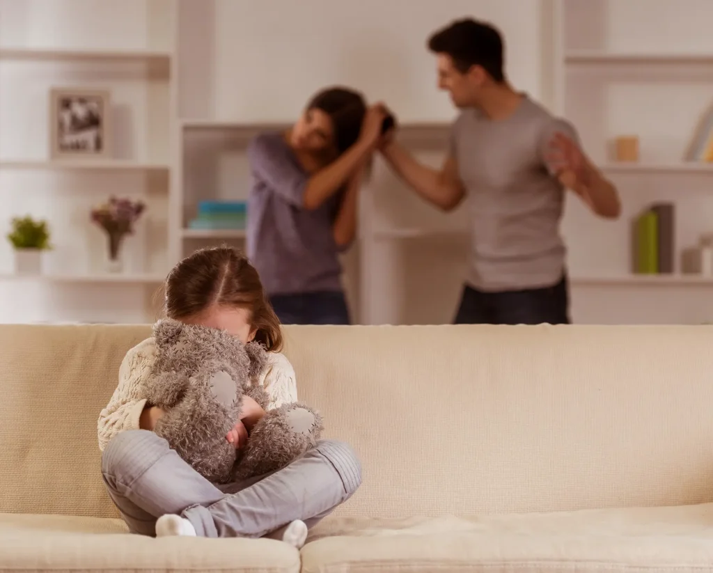 Upset little girl with her face buried in a stuffed animal while her parents are in a physical altercation behind her. If you're facing domestic violence in your marriage, our Oklahoma City family law attorneys can help you safely file for divorce.