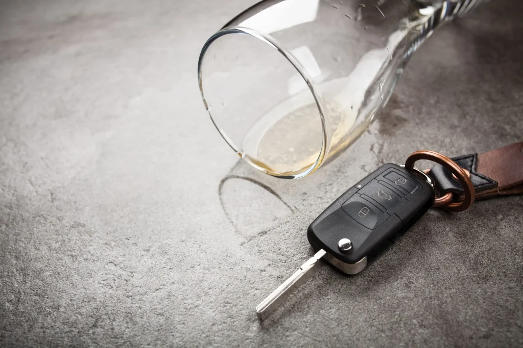 A spilled glass of alcohol next to car keys. If you have been charged with a DUI you may be wondering how to apply for the Oklahoma Impaired Driver Accountability Program (IDAP).