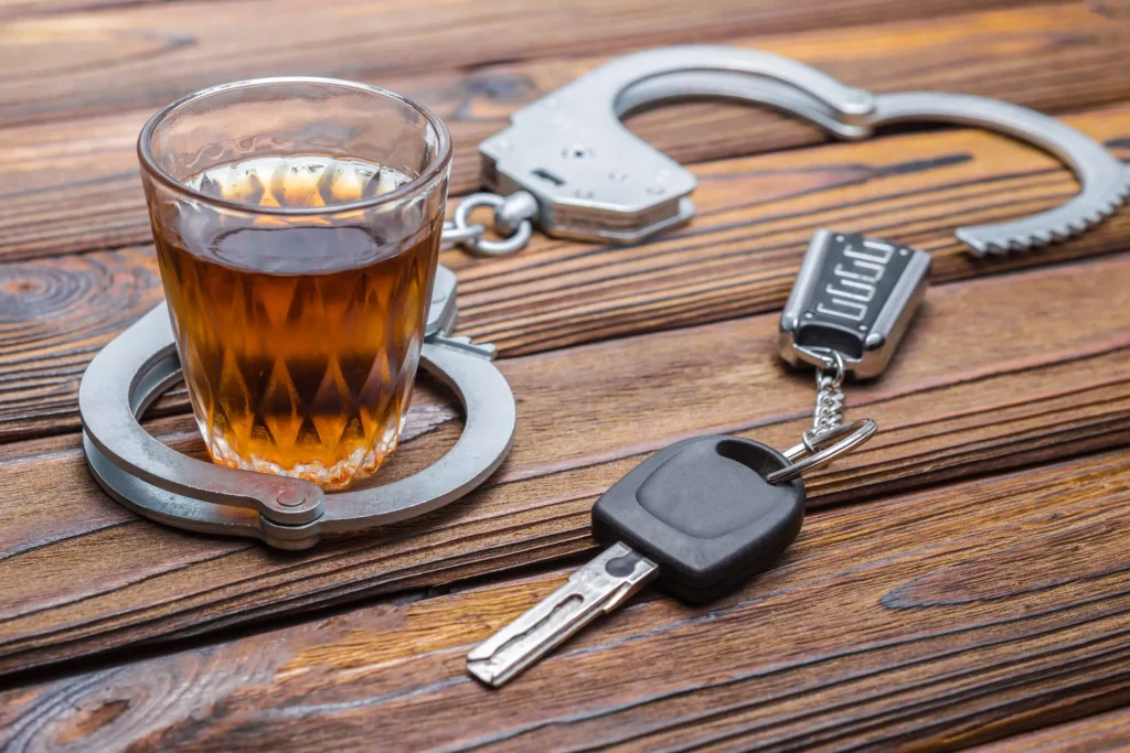 a glass of alcohol, car keys, and a pair of handcuffs