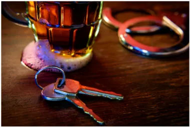 A drink, handcuffs and keys on a bar.