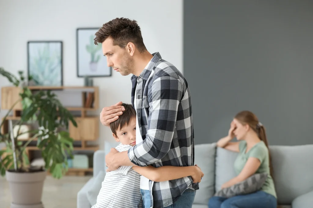 A man hugging his son in front of his angry wife.