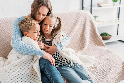 A mom hugging her kids on a couch.