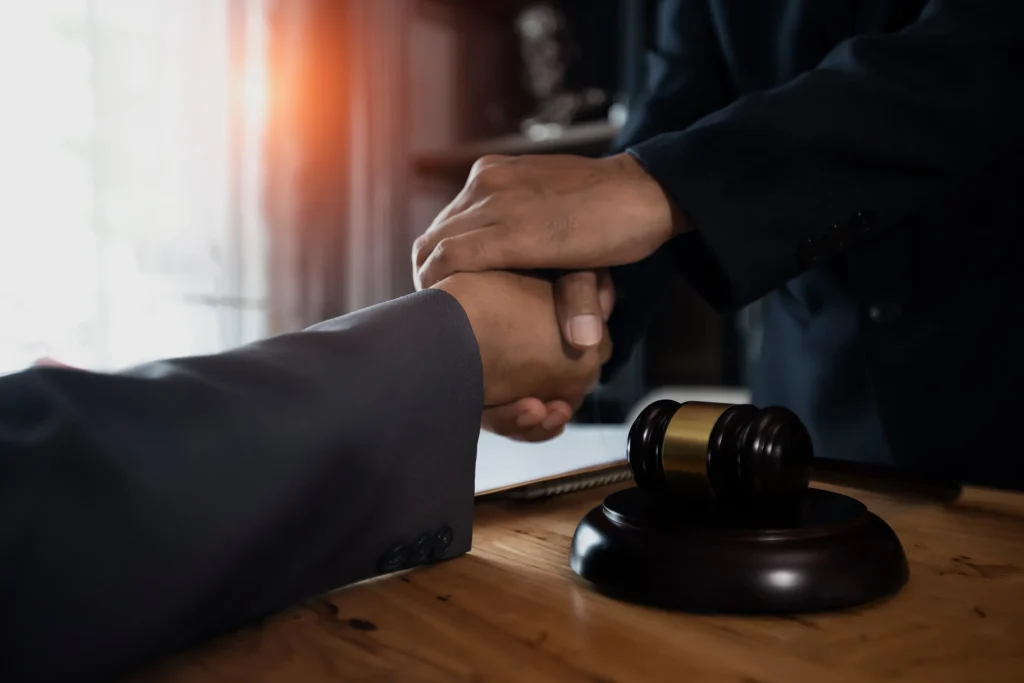 Two people shaking hands over a desk with a gavel on it.