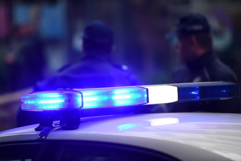 Primer plano de las luces azules de emergencia de una patrulla con dos agentes de policía desenfocados al fondo.