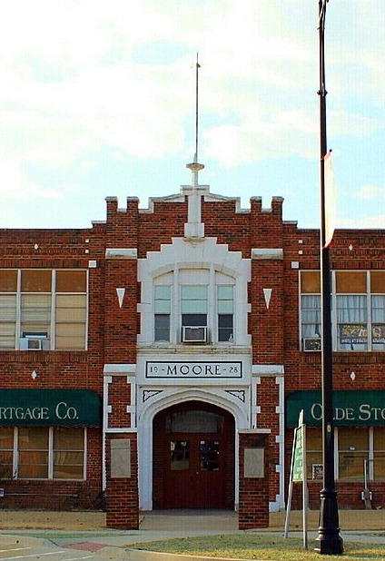 Front entrance of historic 1928 Old Moore High School in Moore, OK. Two-story red-brick façade with white stone arch and “MOORE” nameplate.